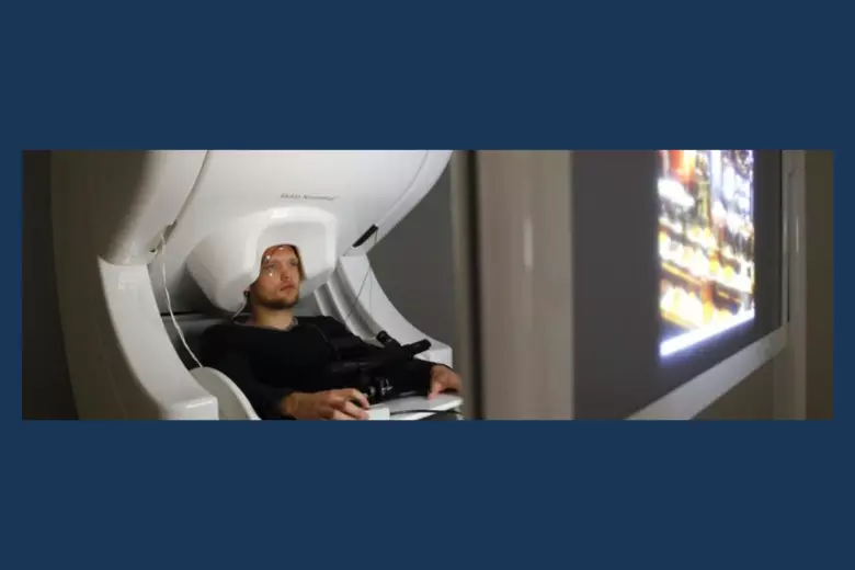 Man sitting under a white MEG machine