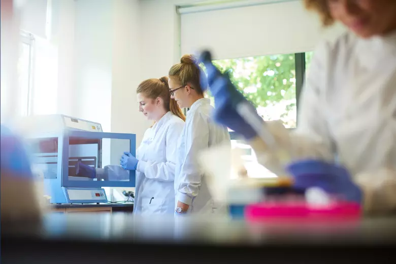Three women in white lab coats doing experiments